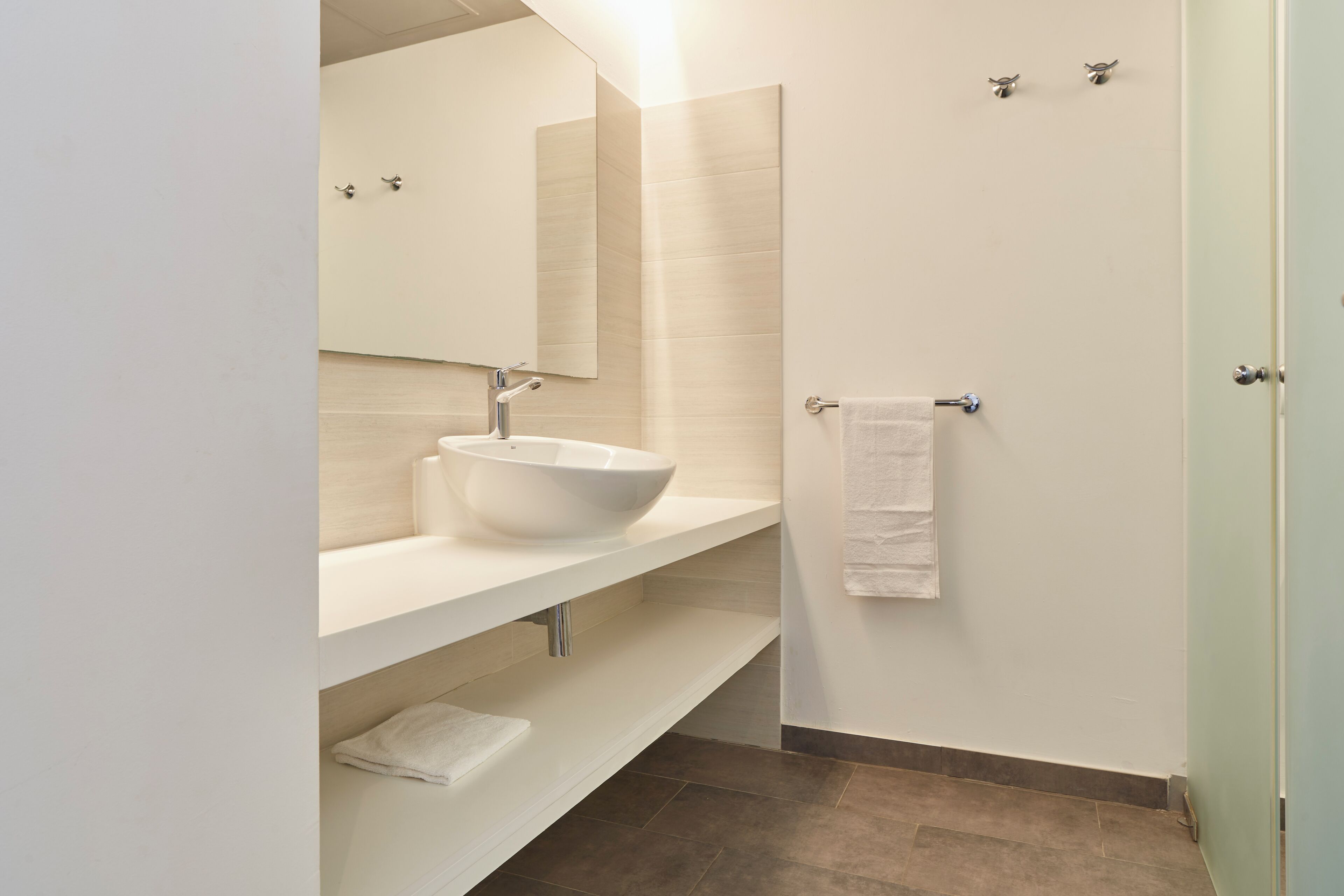 A modern bathroom with a white sink, mirror, and towel rack.