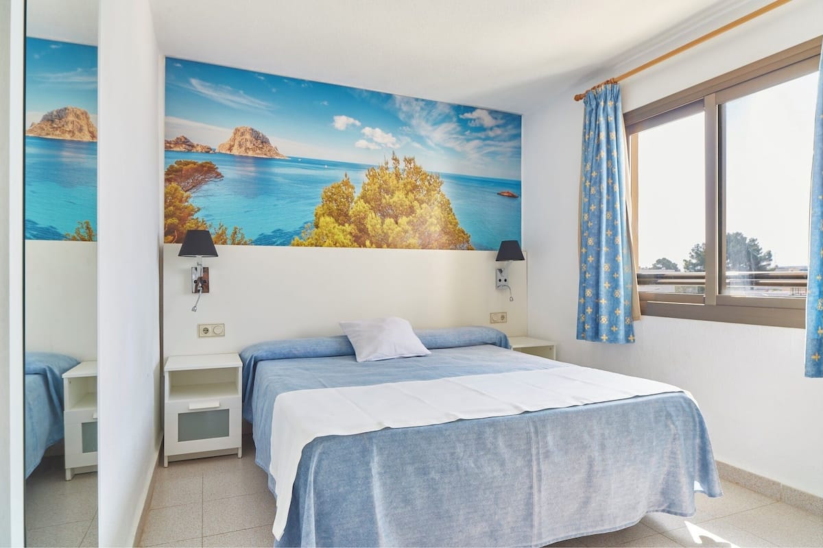 Une chambre à coucher avec un lit, une table de chevet, une lampe et une fenêtre avec des rideaux.