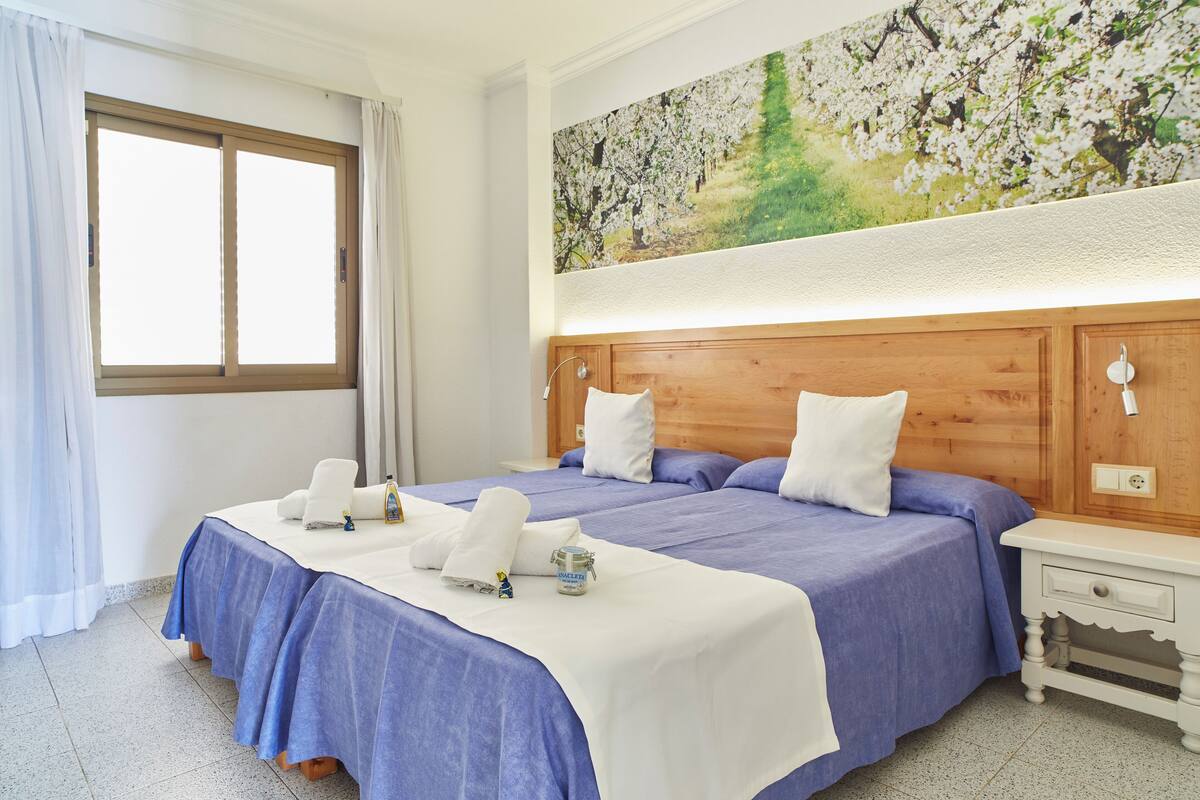 Une chambre d’hôtel avec un grand lit, une tête de lit en bois, une table de chevet et une fenêtre avec des rideaux.