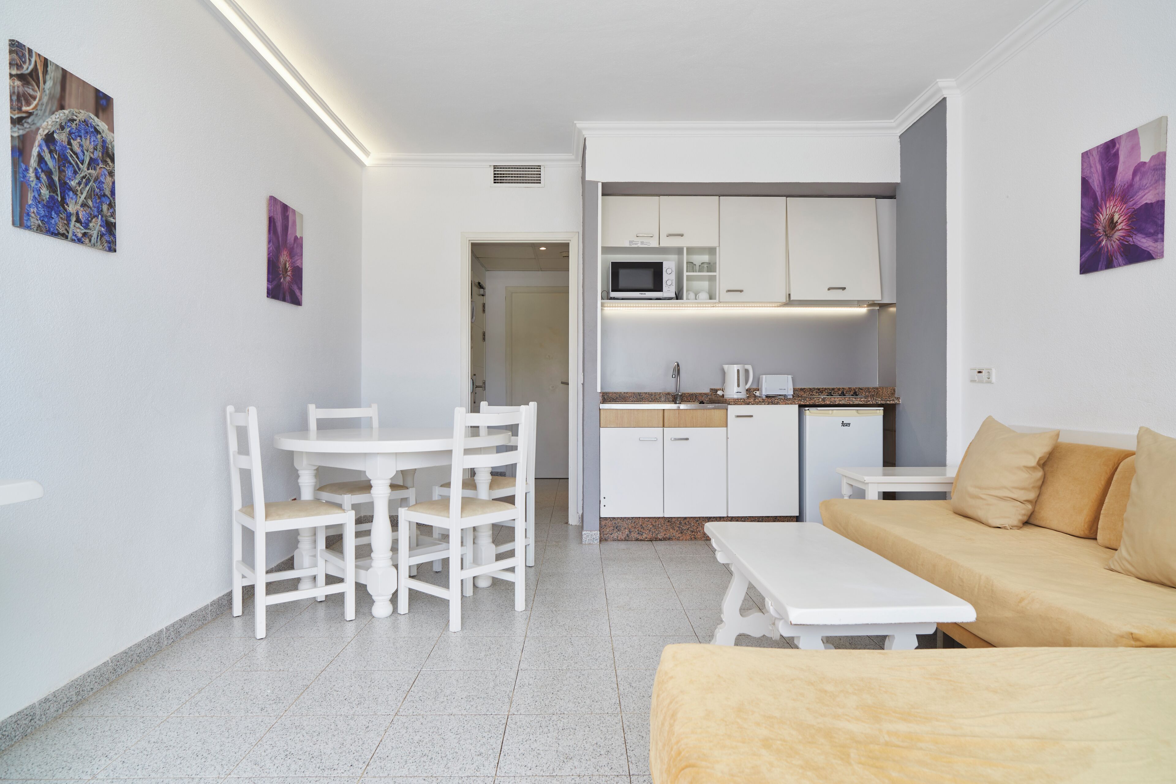 Una habitación compacta con kitchenette, comedor con sillas y mesa, y un sofá.