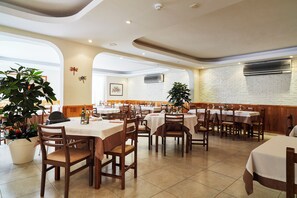 A spacious restaurant with multiple tables and chairs, potted plants, and a brick wall. - Invisa Aparthotel Casa Luis - New opening 2026 (Santa Eulalia del Rio)