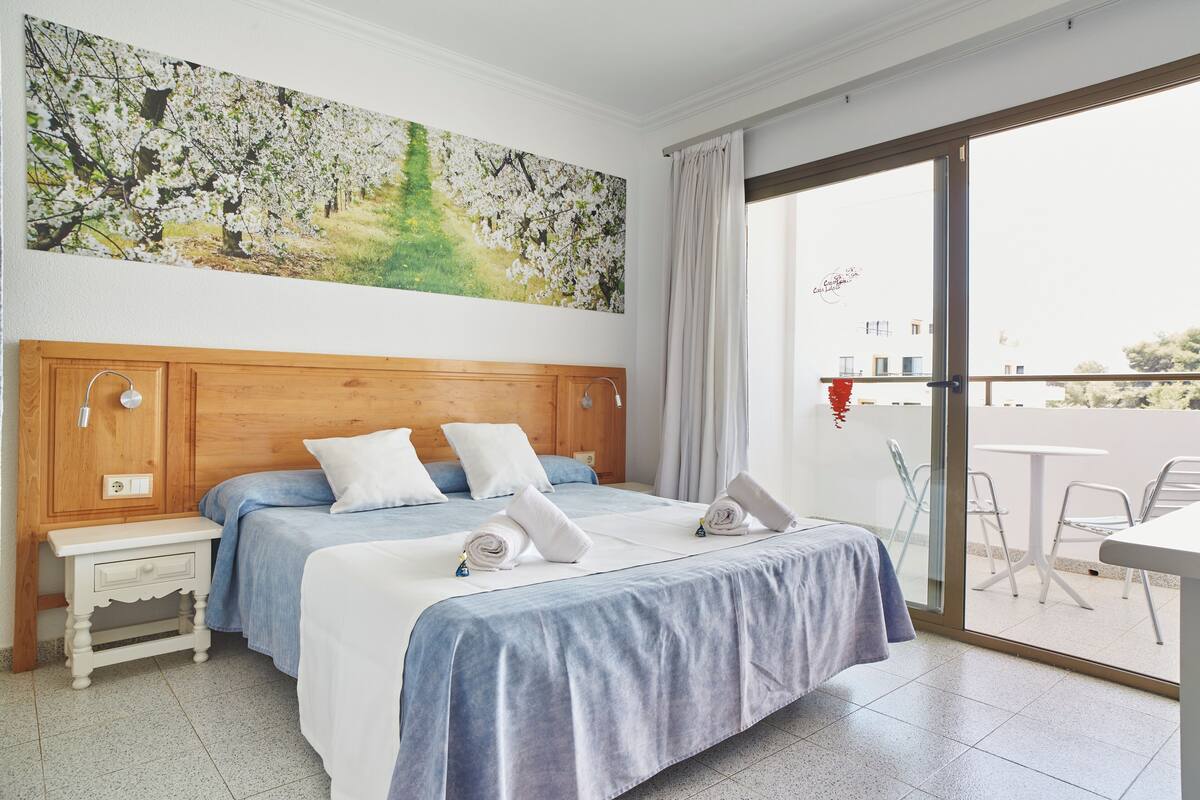 Une chambre d’hôtel avec un grand lit, une tête de lit en bois, une table de chevet et un tableau représentant un arbre.