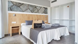 Een moderne slaapkamer met een stenen muur, houten hoofdbord, een nachtkastje, een bed met een grijze deken en een opbergmeubel.