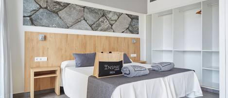 A modern bedroom with a stone wall, wooden headboard, a bedside table, a bed with a grey blanket, and a storage unit.