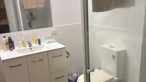 A bathroom with a white sink, mirror, and toilet. There is a shower area with a glass door and a towel hanging on it. - Fantastic location townhouse close to beaches , shops , bus stop (Runaway Bay)