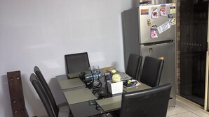 A dining area with a glass-top table, black chairs, and a refrigerator with magnets. - Fantastic location townhouse close to beaches , shops , bus stop (Runaway Bay)