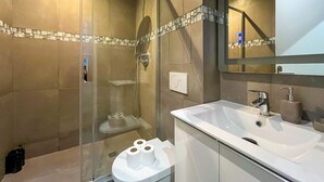 Ein modernes Badezimmer mit einer begehbaren Glasdusche, einem weißen Waschbecken und einem Spiegel.