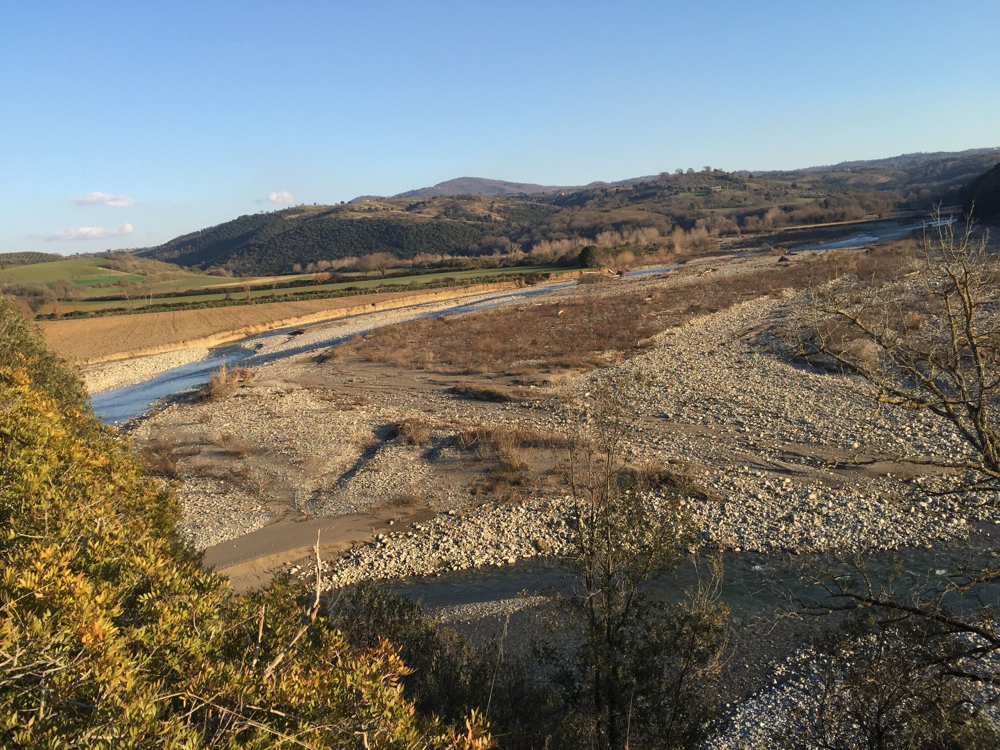 Een rivier die door een valleigebied stroomt met rotsachtig terrein en schaarse begroeiing.