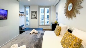 A modern hotel room with a bed, a TV, a sunburst mirror, and a balcony view. - UrbanFlat 206 - 249 Saint Denis SD1 (París)
