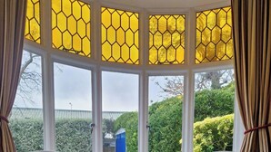 A room with two armchairs, a small round table, and a bay window with yellow-tinted glass. - Admiral’s Rest – Spacious - Historic Georgian Charm in the Heart of Broadstairs with Private Parking (Broadstairs)