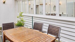 A wooden table with four chairs, a potted plant, and a white exterior wall with windows and wall-mounted lights. - Admiral’s Rest – Spacious - Historic Georgian Charm in the Heart of Broadstairs with Private Parking (Broadstairs)