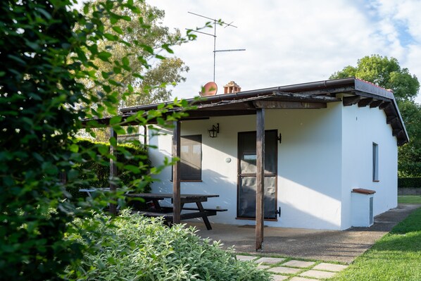 Un piccolo edificio bianco con un portico coperto, un tavolo da picnic e un camino.