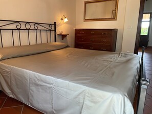 Un letto con testiera, un comodino con lampada, una cassettiera e uno specchio appeso al muro.