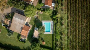 An aerial view of a residential property with a swimming pool, a fenced garden, and a field.