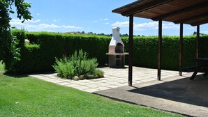 A patio area with a chimney, a covered seating area, and a hedge in the background.