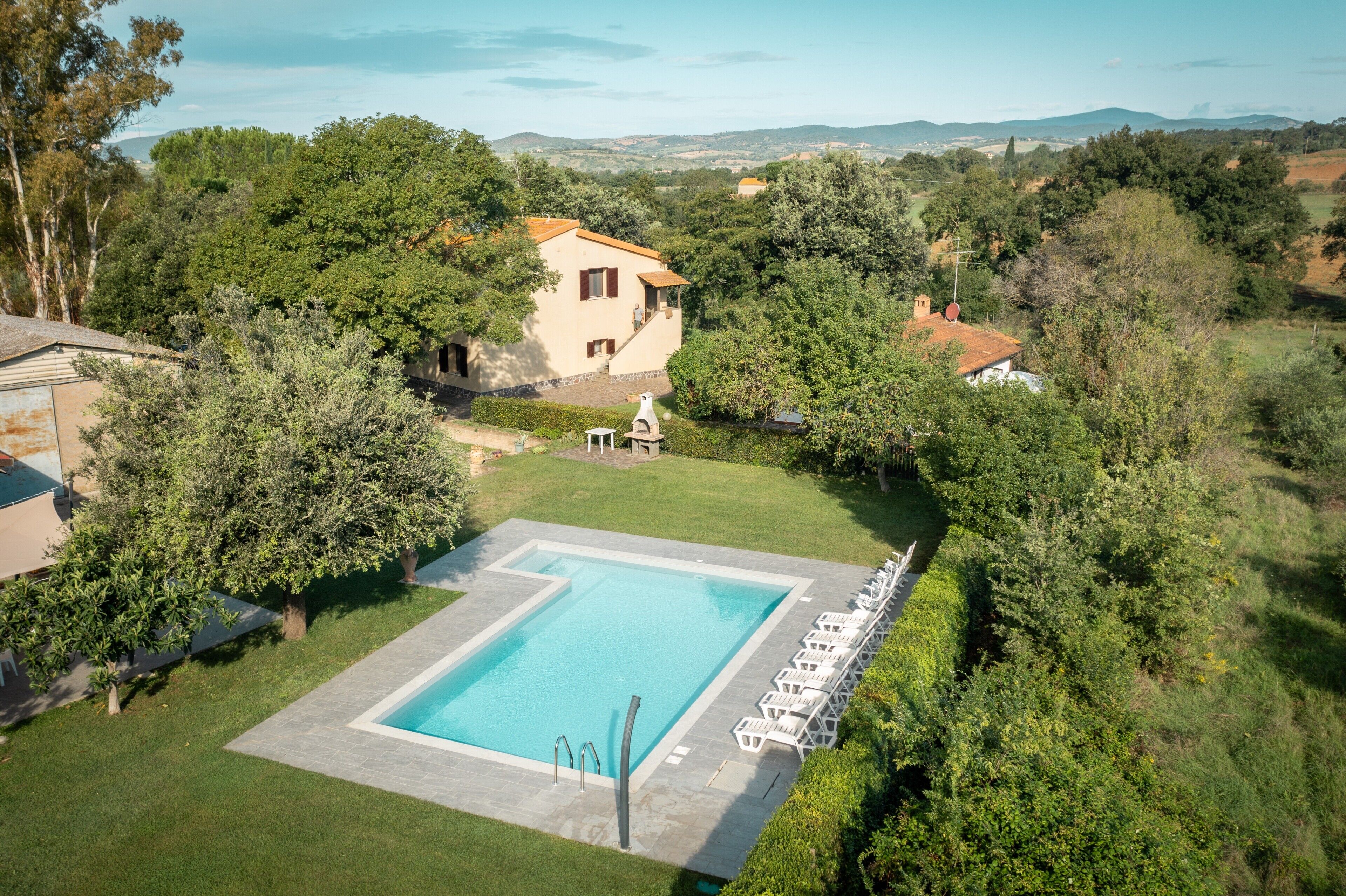 Piscina com espreguiçadeiras, cercada por vegetação e uma casa ao fundo.
