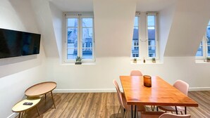 Et moderne spiseområde med et træbord og stole, et fladskærms-tv på væggen og to vinduer med plantekasser.
