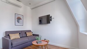En moderne stue med en grå sofa, et rundt træbord og et vægmonteret fladskærms-tv.