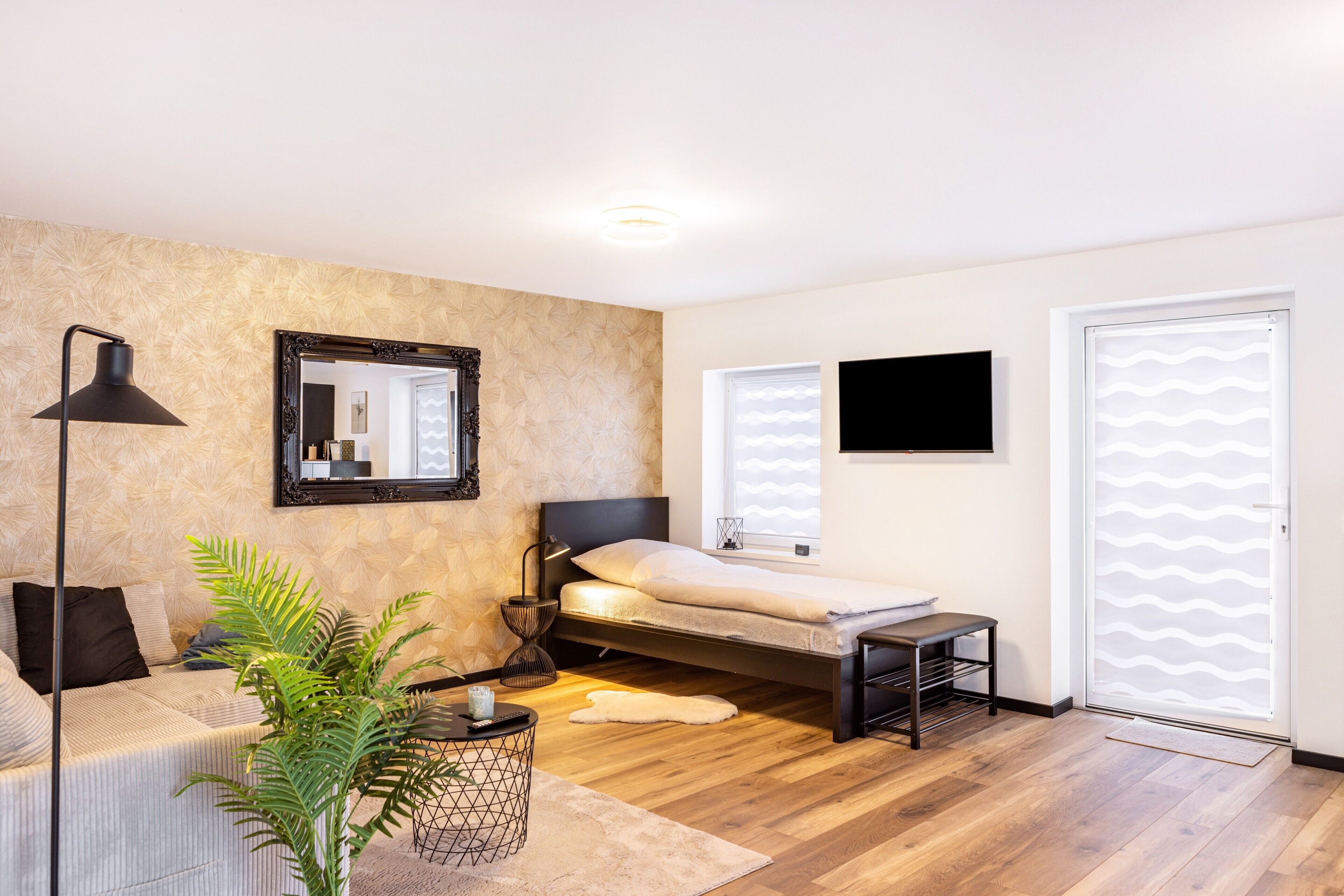 Un dormitorio con cama, mesita de noche, lámpara, espejo y una planta en maceta.