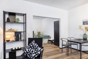 Una sala de estar moderna con un sofá negro, una mesa de comedor con sillas, una estantería negra y una pintura de un paisaje urbano en la pared.