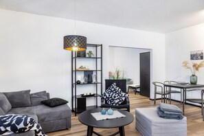 Una sala de estar moderna con un sofá, una mesa redonda para café, una estantería, un área de comedor con sillas y una lámpara colgante.