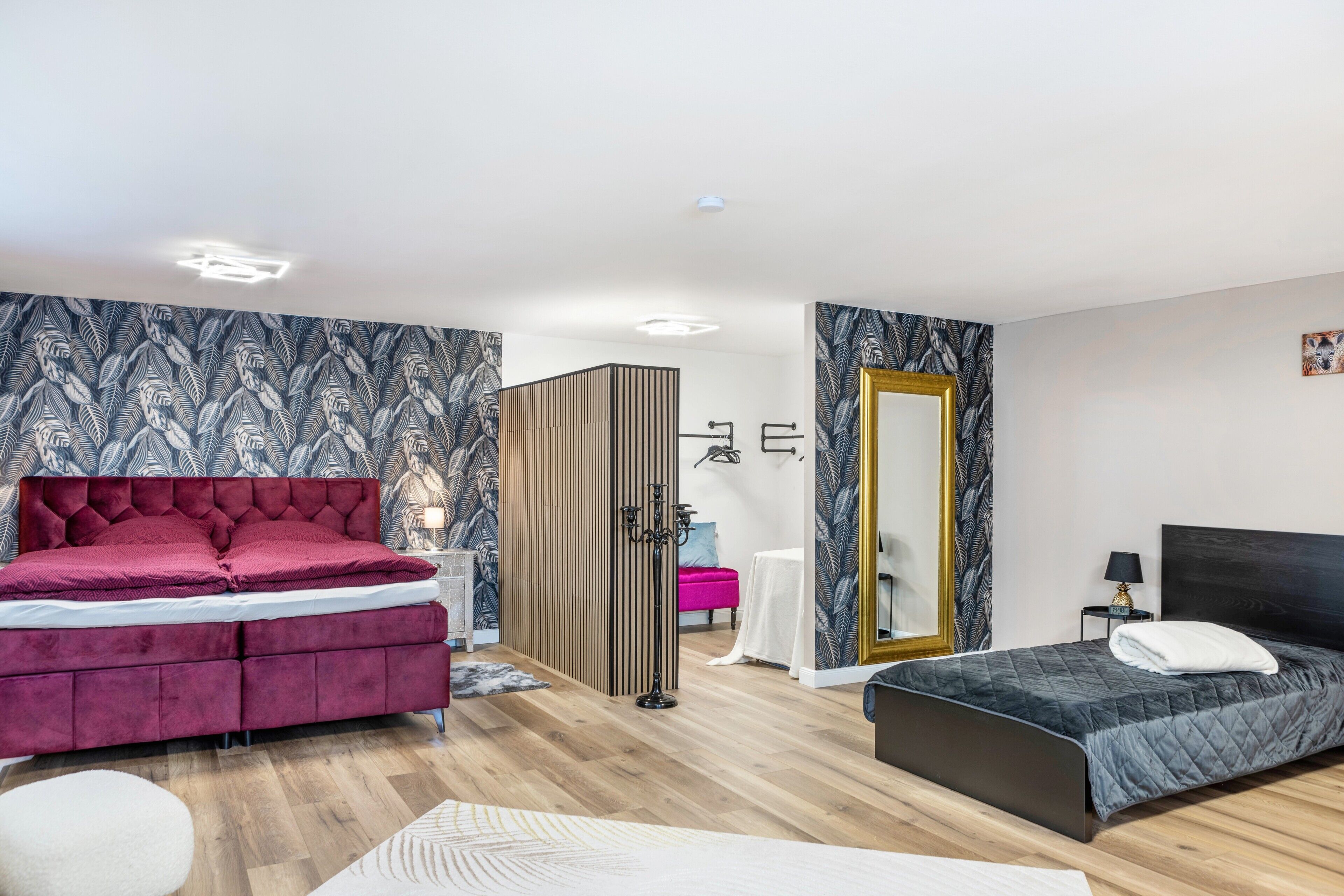 A modern bedroom with a large bed, a smaller bed, a wardrobe, a mirror, and a nightstand.