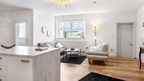 Ein modernes Wohnzimmer mit einer Marmorküche mit Kochinsel, einem Sofa, einem Couchtisch und einem Esstisch.