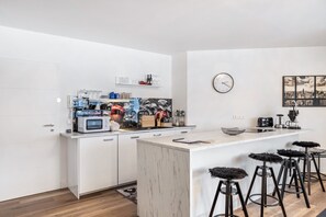 Una cucina moderna con mobili bianchi, un'isola in marmo, sgabelli da bar, un orologio e un'opera d'arte raffigurante un panorama cittadino.