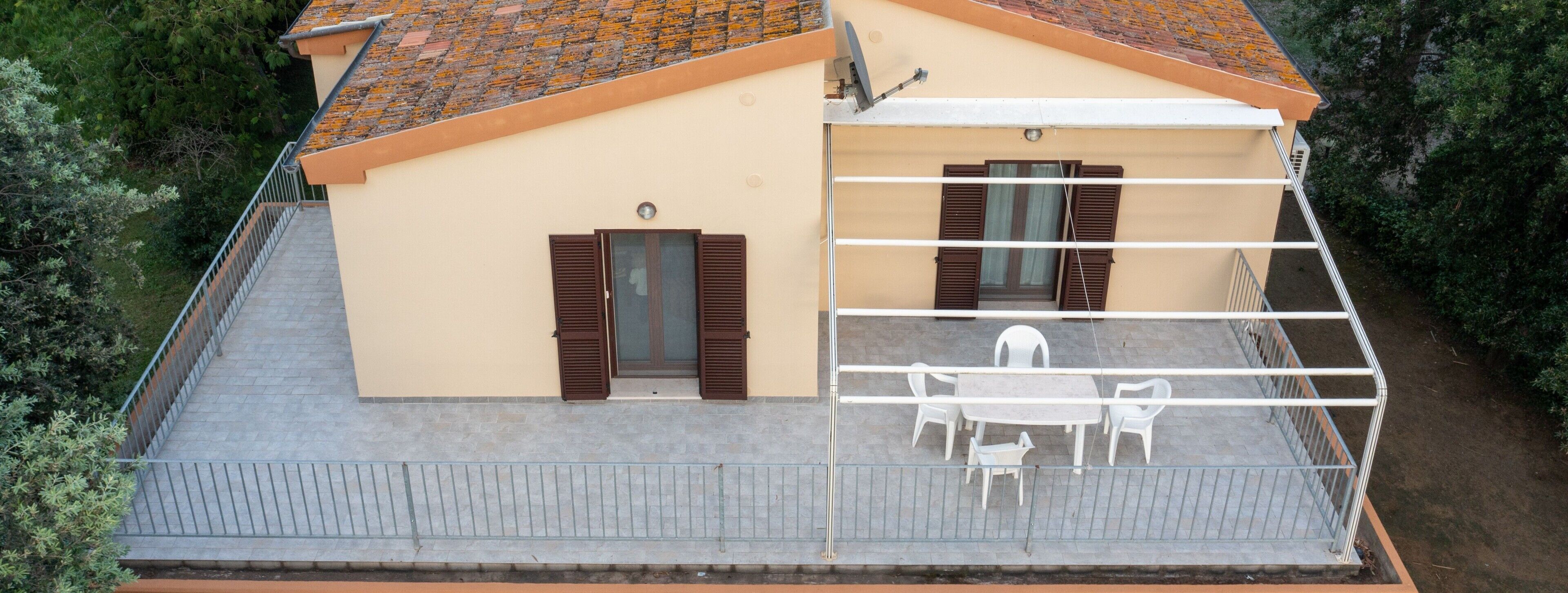 A two-story building with a balcony, a satellite dish, and a small outdoor seating area with chairs.