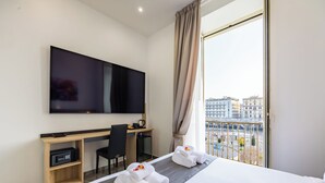 A hotel room with a bed, a desk, a chair, a flat-screen TV, and a view of the city through a large window. - Sant'Angelo Station (Naples)
