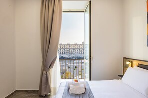 A hotel room with a bed, a nightstand, a window with curtains, and a view of a cityscape. - Sant'Angelo Station (Naples)
