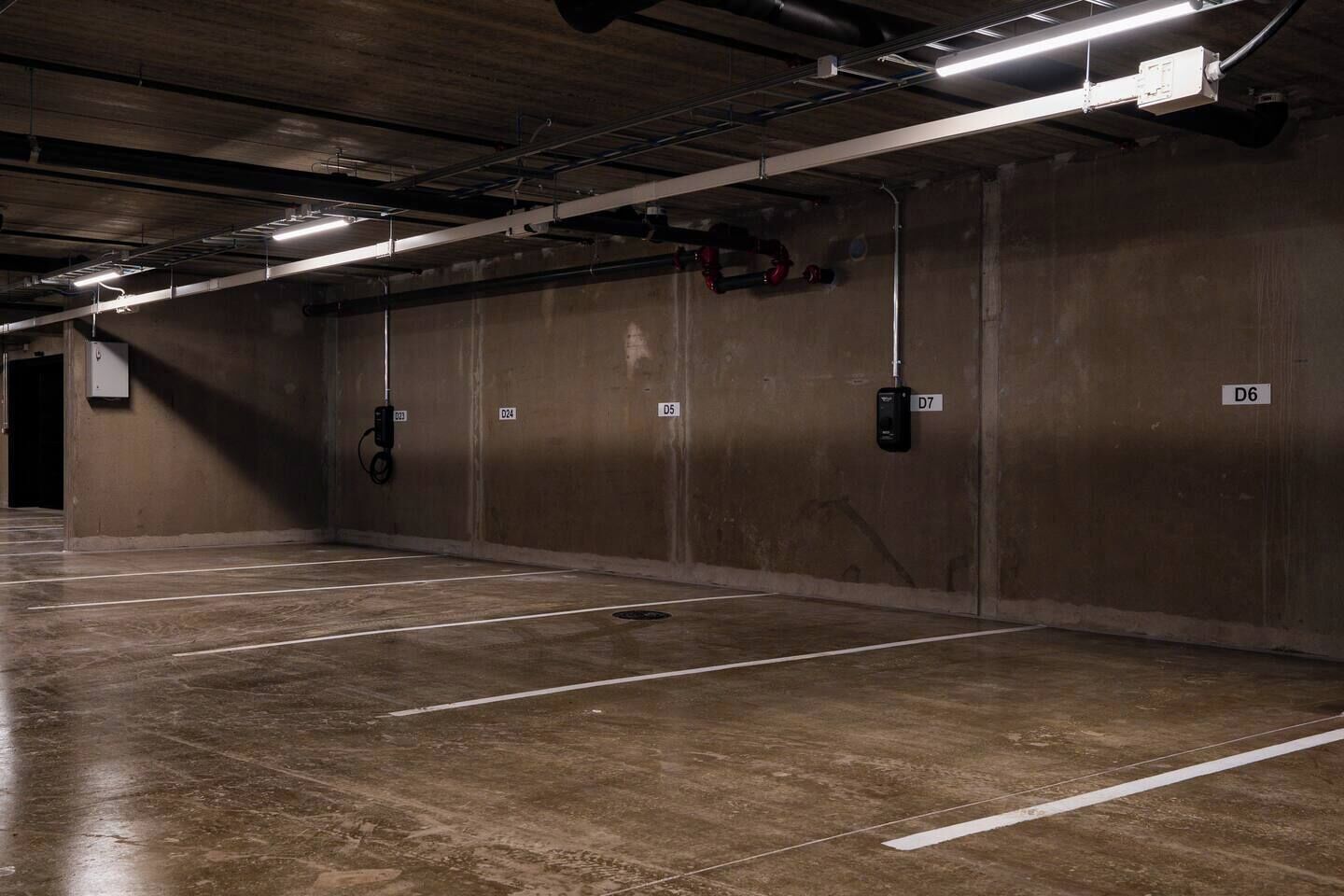Un parking souterrain aux murs et au sol en béton, doté de places de stationnement numérotées et d’un éclairage au plafond.