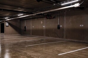 A parking garage with concrete walls and floors, numbered parking spaces, and overhead lighting. - Central Lux Apartment D19 by Aavalevi (Levi)
