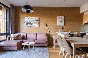 A modern living room with a sectional sofa, a small round table, and a dining area with a long table and chairs. - Central Lux Apartment D19 by Aavalevi (Levi)
