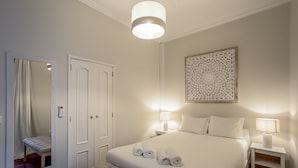 Un dormitorio ordenado con una cama grande, mesitas de noche con lámparas, un espejo y un adorno decorativo en la pared.