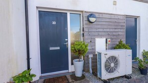 Un bâtiment avec une porte bleu foncé portant le numéro 33, une petite plante en pot et un appareil de climatisation installé à l’extérieur.