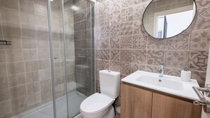 A bathroom with a glass shower enclosure, a white toilet, a sink with a mirror above it, and patterned wall tiles. - Braga Essence Studio by Minhos Guest (Braga)