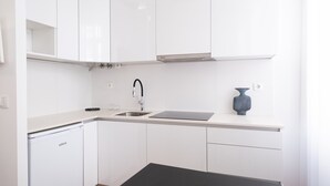 A modern kitchen with white cabinets, a dishwasher, a sink, and a vase on the countertop. - Braga Essence Studio by Minhos Guest (Braga)