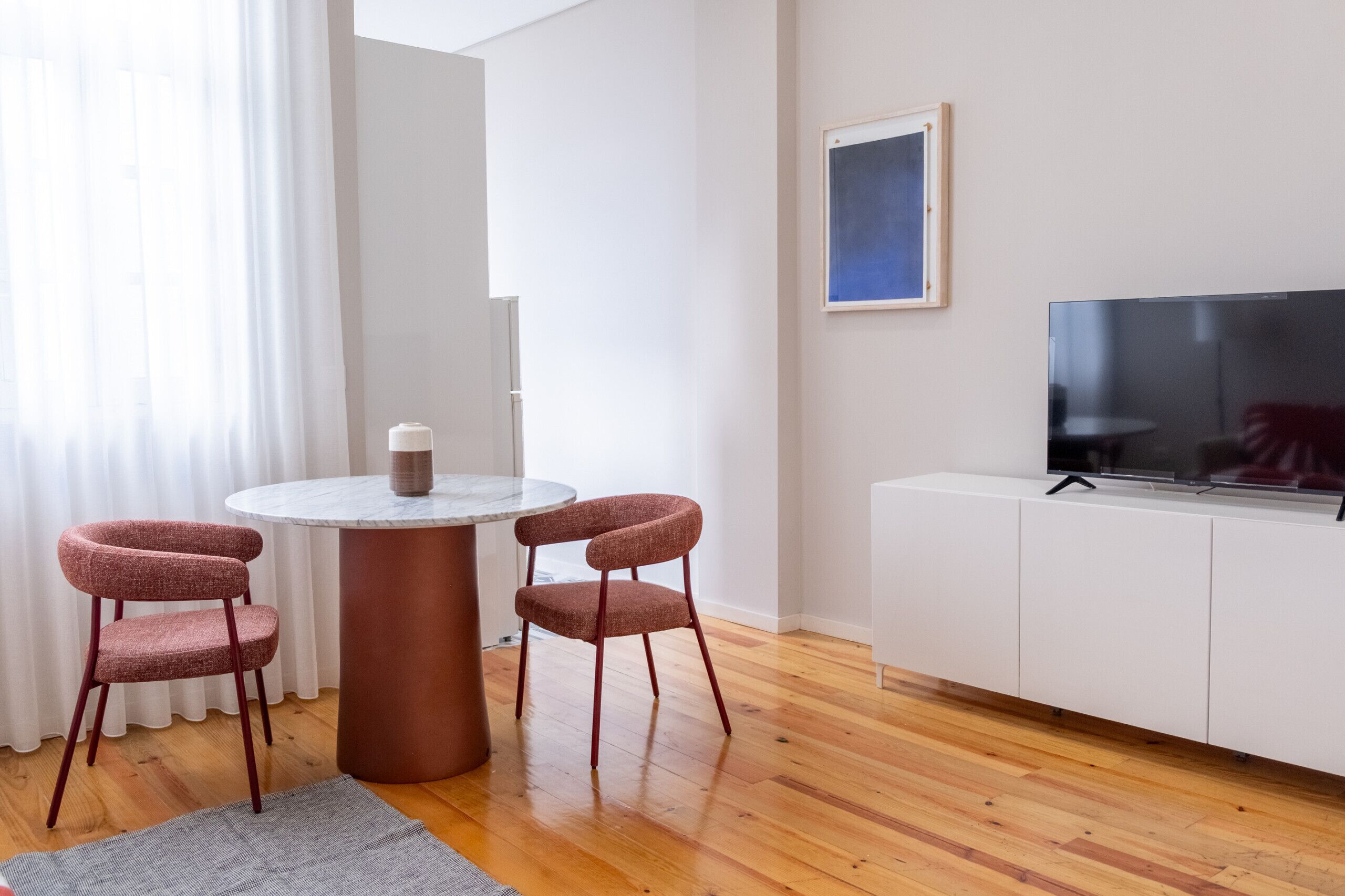 Ein modernes Wohnzimmer mit einem runden Tisch, zwei roten Sesseln, einem weißen Schrank und einem Flachbildfernseher.