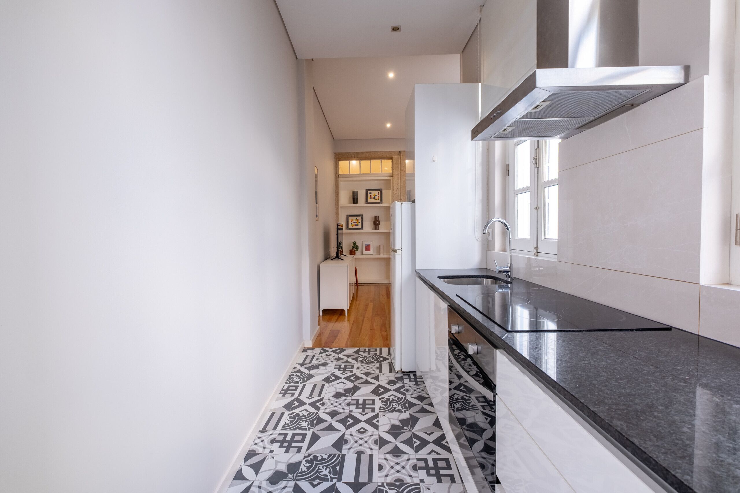 A narrow kitchen with a black countertop and patterned floor tiles.