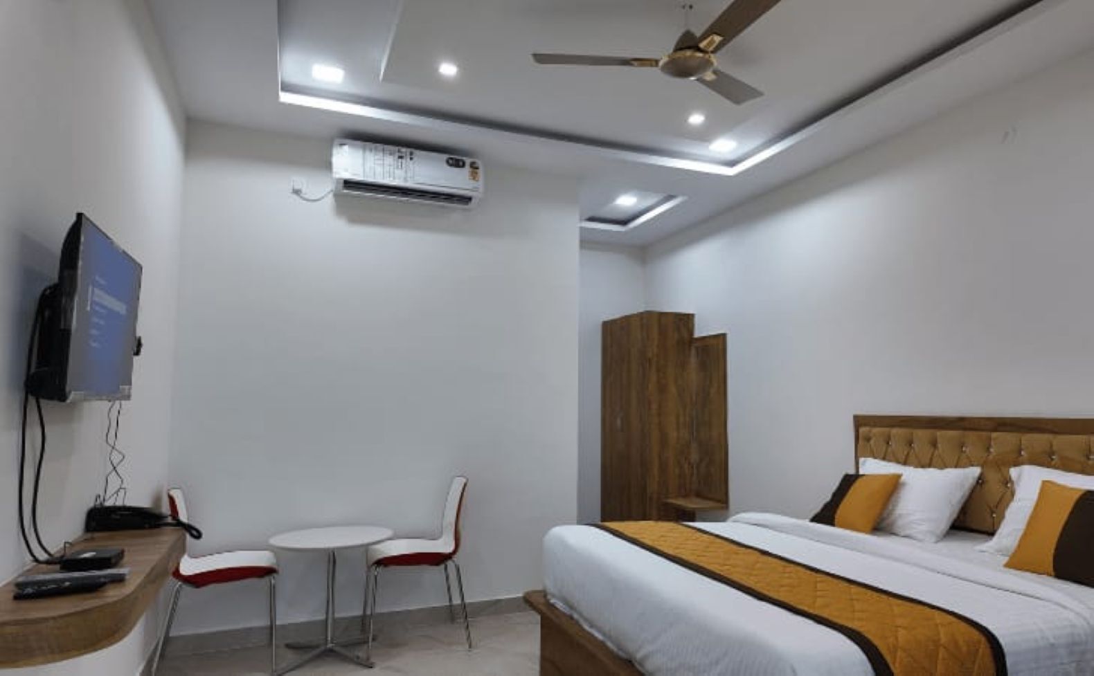 Una habitación de hotel con cama, televisión, escritorio y silla, y un ventilador de techo.