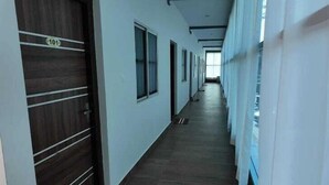 A long, narrow hallway with wooden doors on the left and windows on the right. - BR Comfort (Bengaluru)