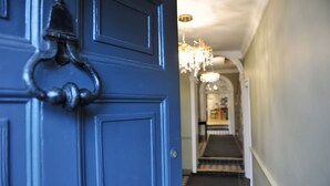 Una porta blu con un maniglione in metallo, che dà su un corridoio con un lampadario e un pavimento tappezzato.