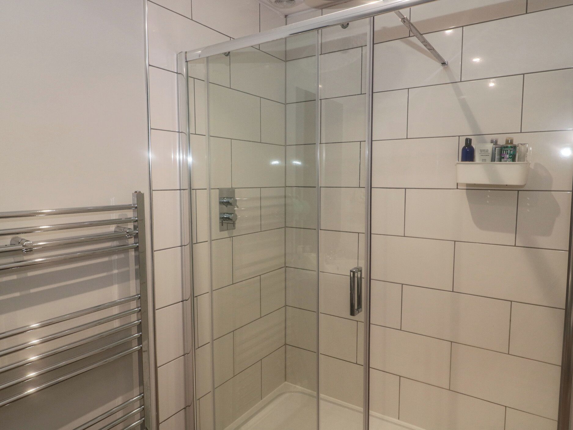 A glass-enclosed shower with a chrome towel rack and a white tiled wall.