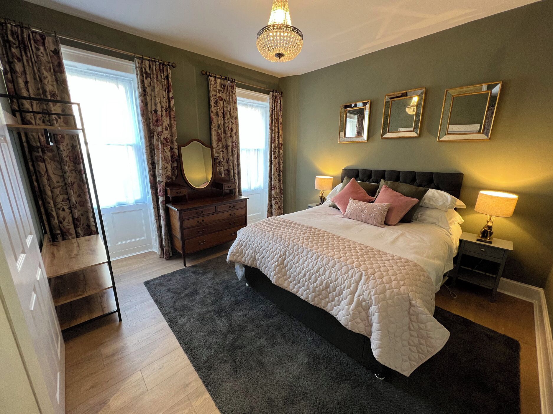 A bedroom with a large bed, a dresser, a vanity with a mirror, and a chandelier.