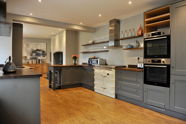 A modern kitchen with grey cabinetry, wooden countertops, and built-in appliances including a stove, oven, and microwave.