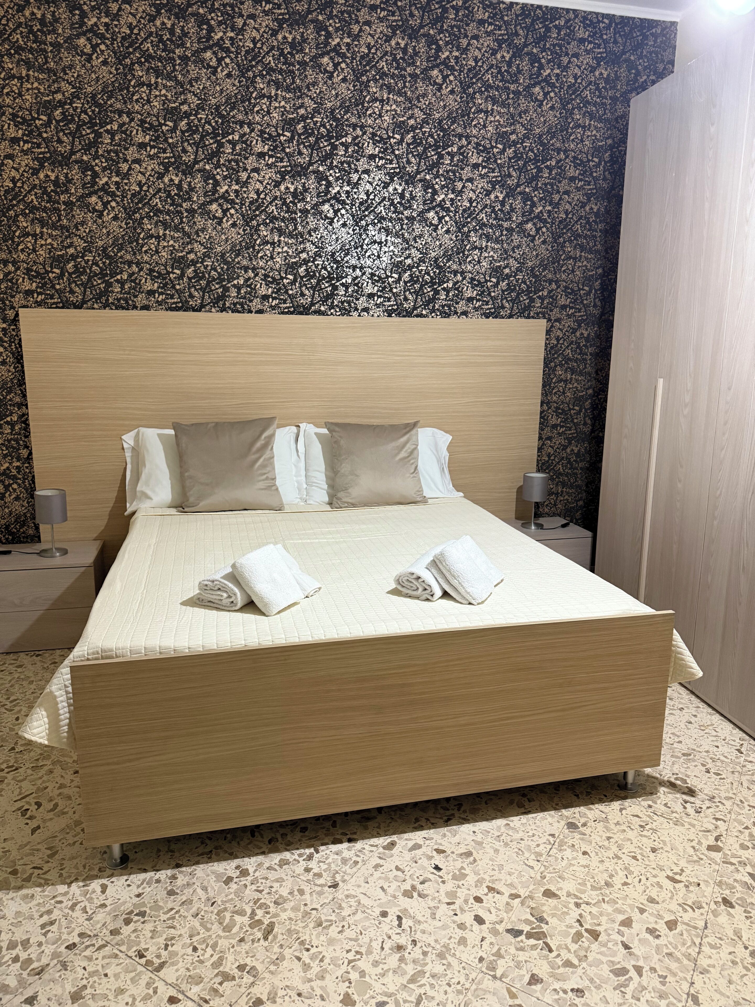 A bed with a wooden headboard, two pillows, and two rolled towels.
