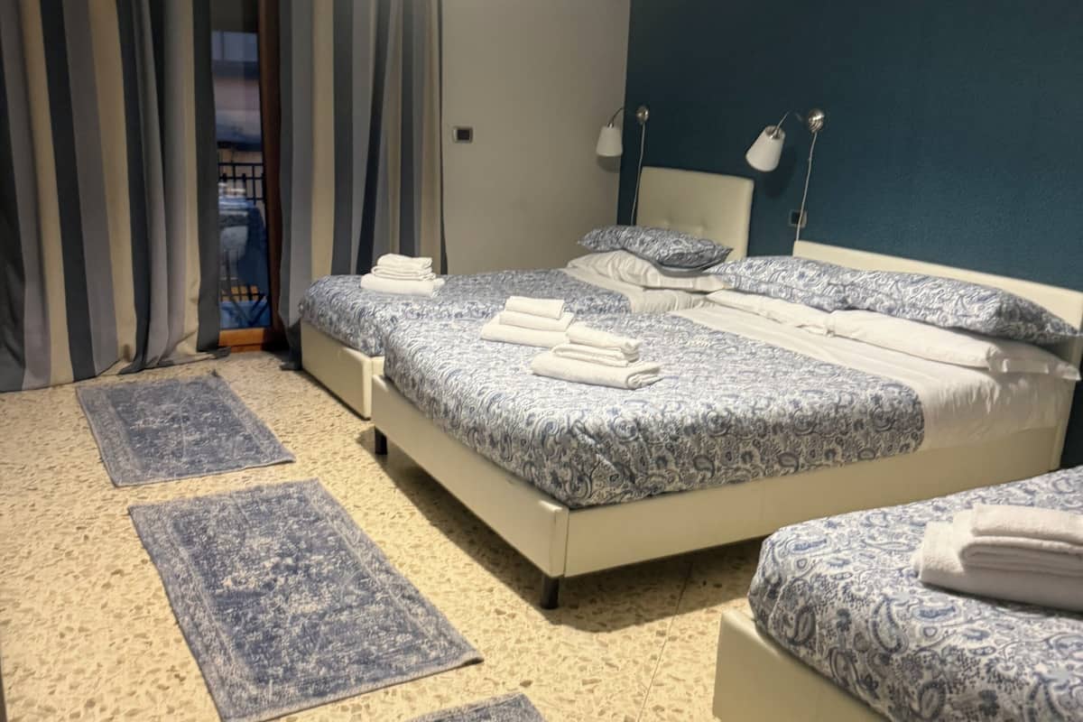 Habitación de hotel con dos camas, un ventanal con cortinas, una lámpara de pie y piso alfombrado.