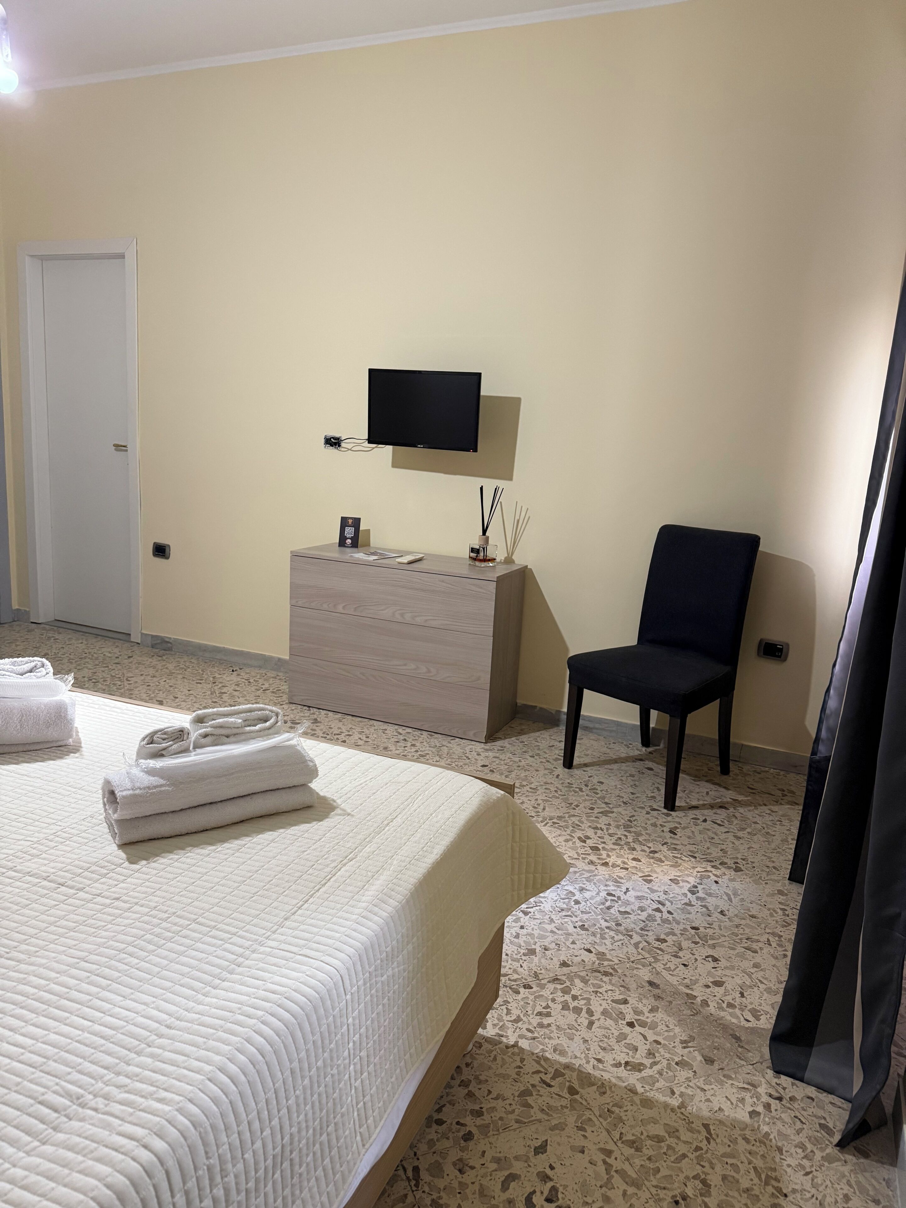Una habitación de hotel con cama, cómoda, silla, televisor y puerta.
