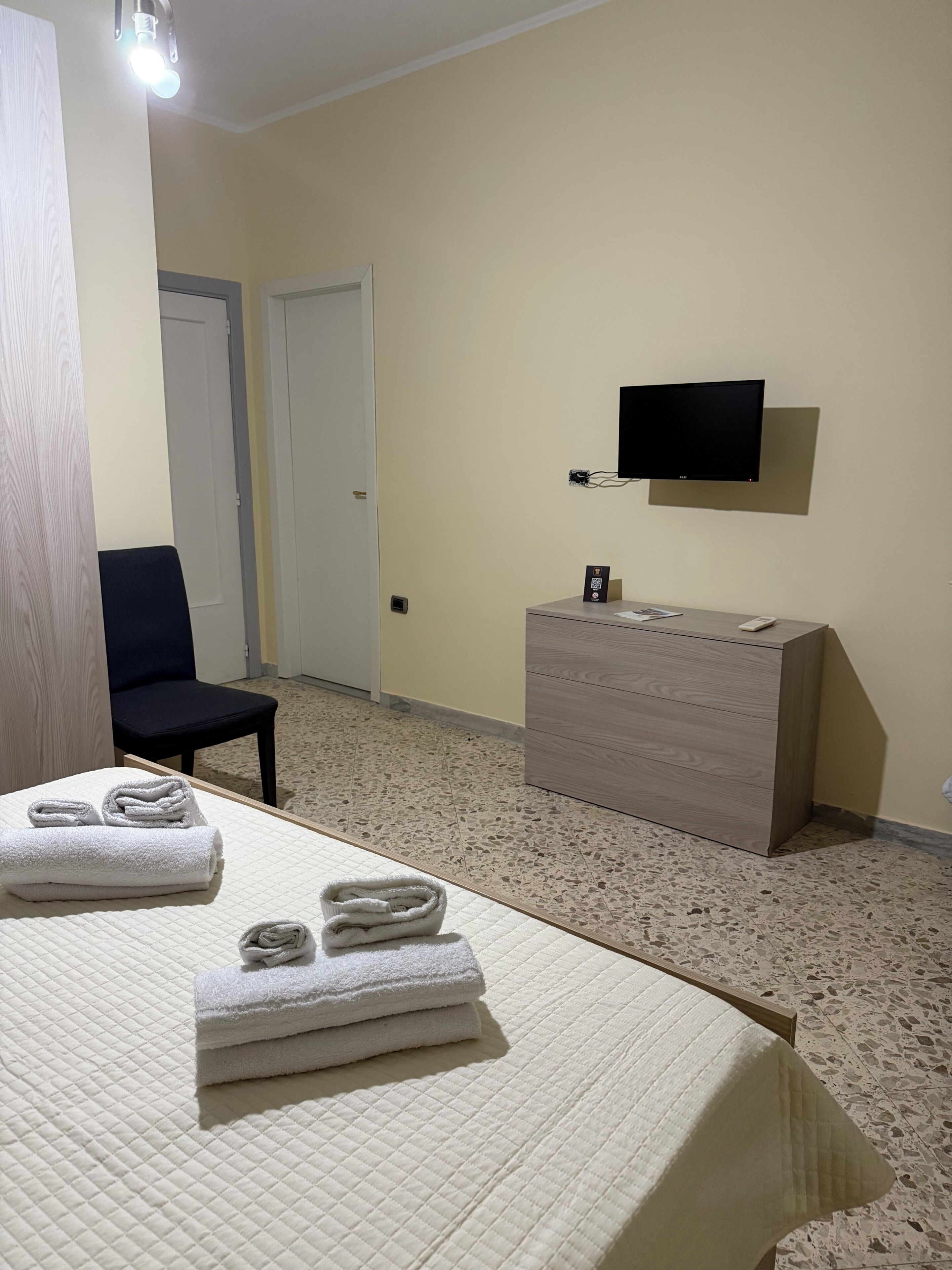 Una habitación de hotel con una cama, una silla, un tocador, un televisor y una puerta.